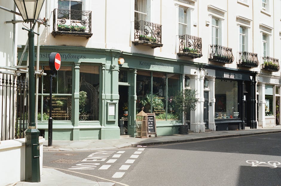 A storefront of a florist shop on Ruislip High Street, painted in soft pastel green with large glass windows displaying lush floral arrangements inside. The shop has a small blackboard sign outside ad